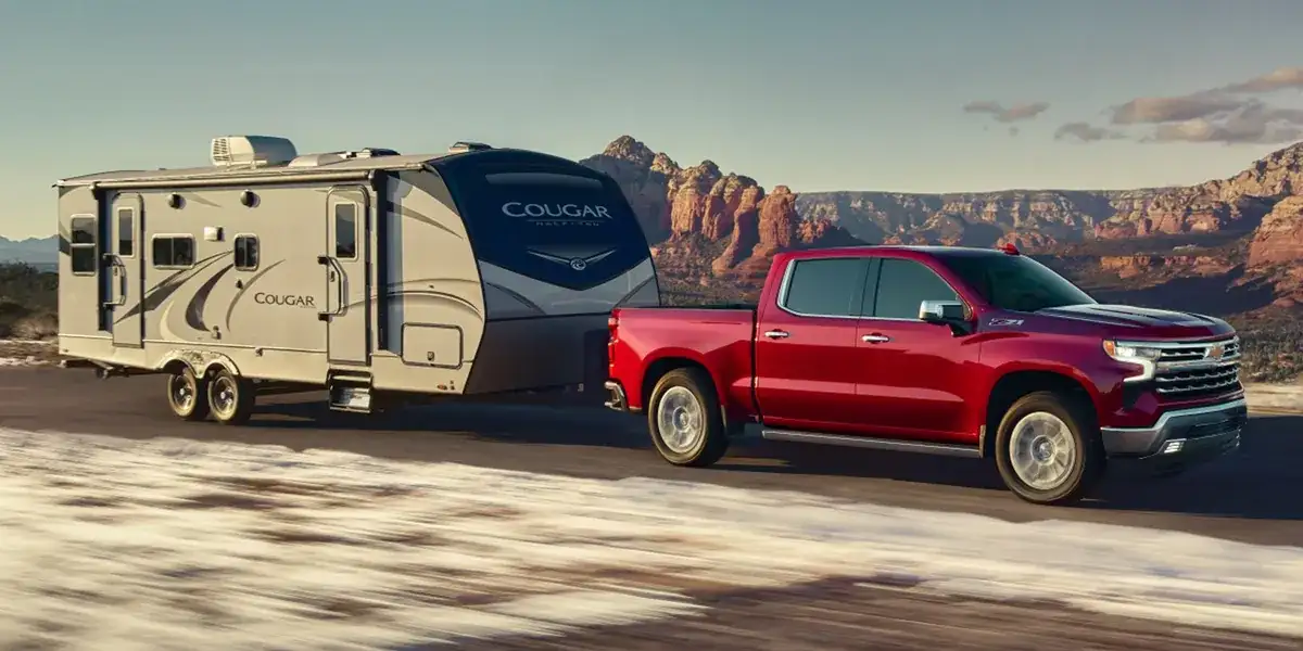 Red 2026 Chevrolet Silverado 1500 towing a travel trailer on a desert road