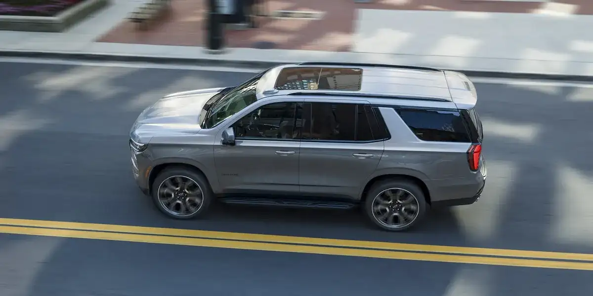 Silver 2027 Chevrolet Tahoe driving on a two-lane road seen from above