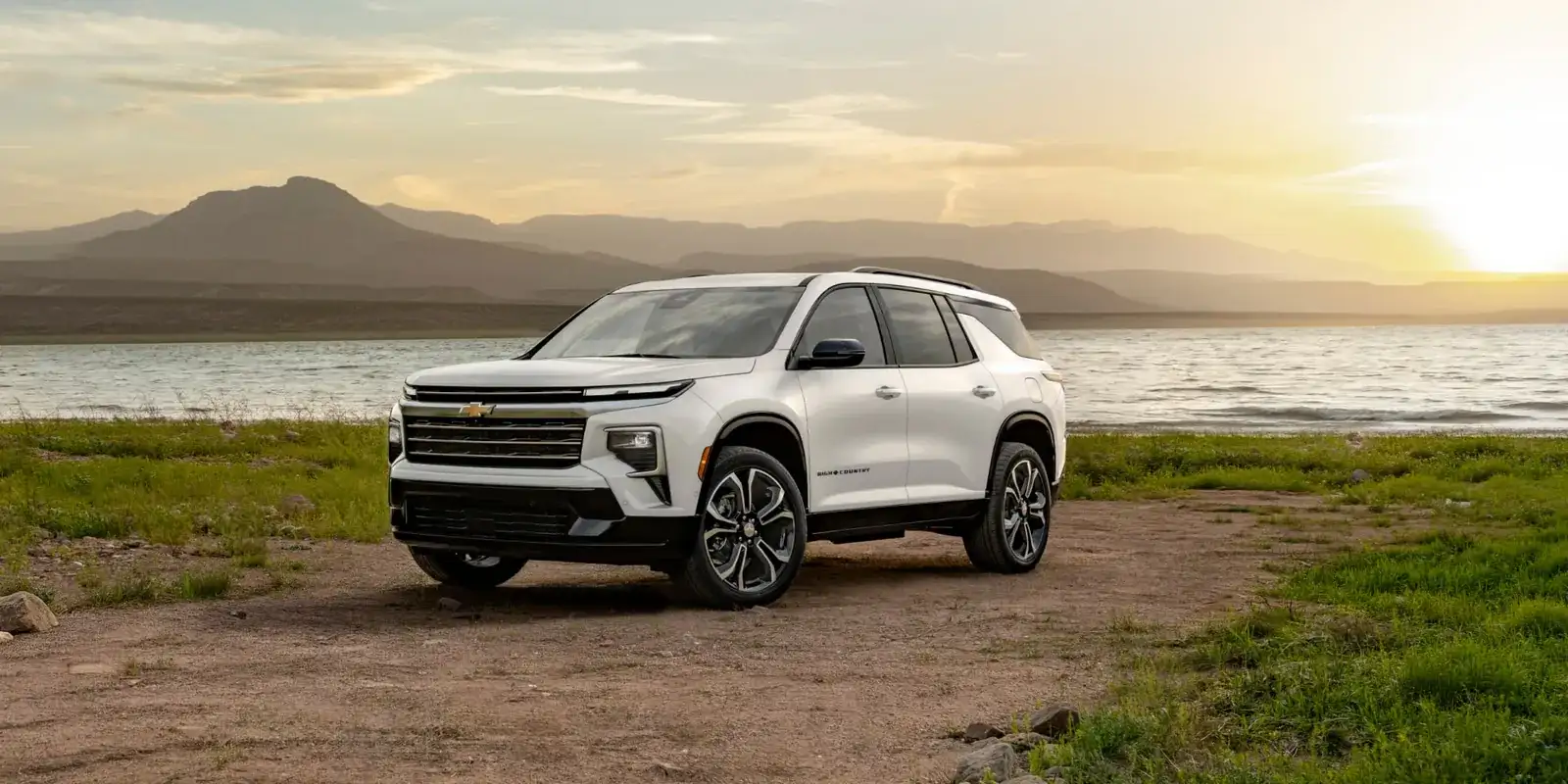 White 2027 Chevrolet Traverse parked by a lake with hills at sunset