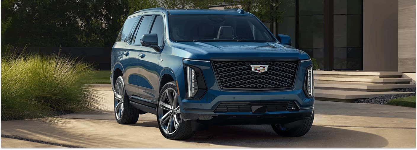 Front three-quarter view of a blue 2026 Cadillac Escalade parked on a paved residential driveway.