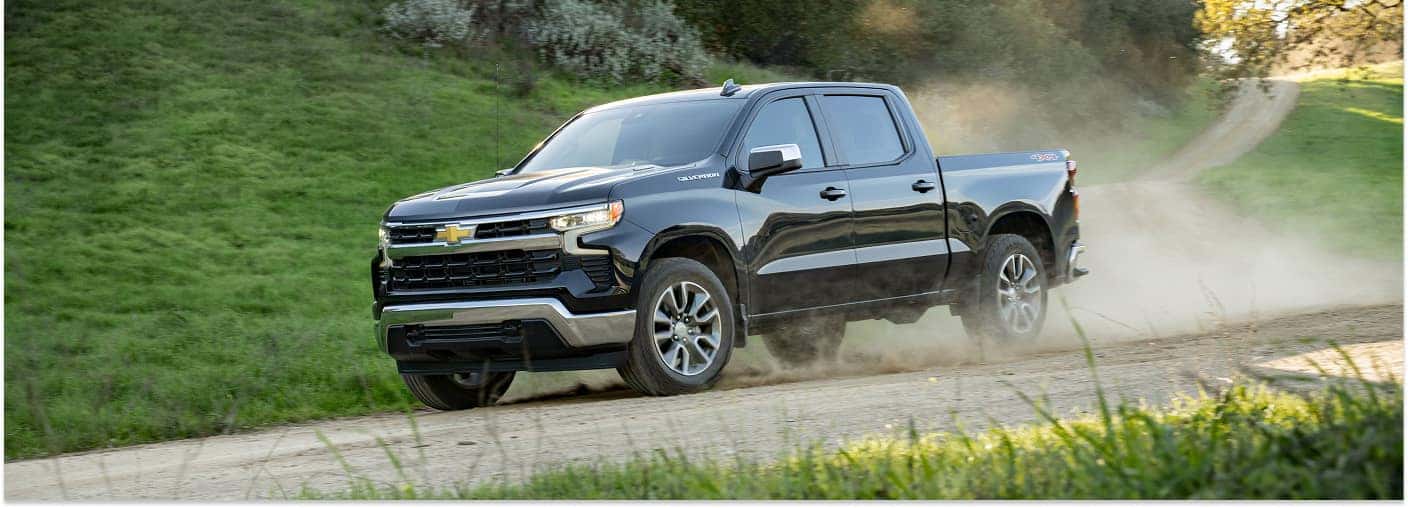 Black 2026 Chevrolet Silverado 1500 pickup truck driving on a dirt road in front three-quarter view.