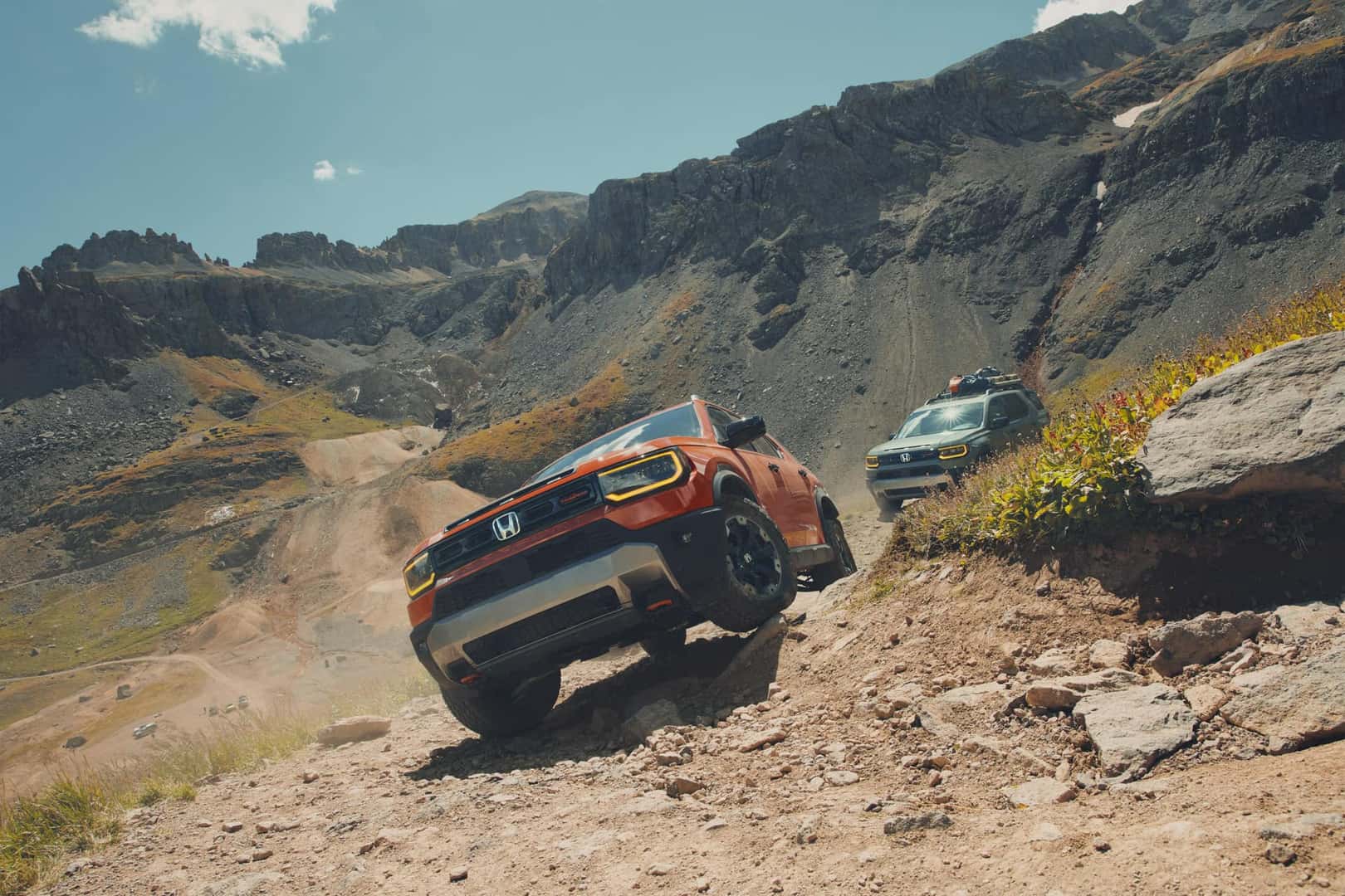 2026 Honda Passport Sunset Orange parked on rocky mountain terrain surrounded by desert landscape