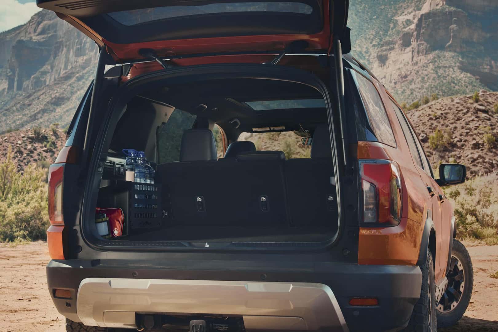 2026 Honda Passport Sunset Orange with rear cargo hatch open displaying trunk storage capacity in mountain setting