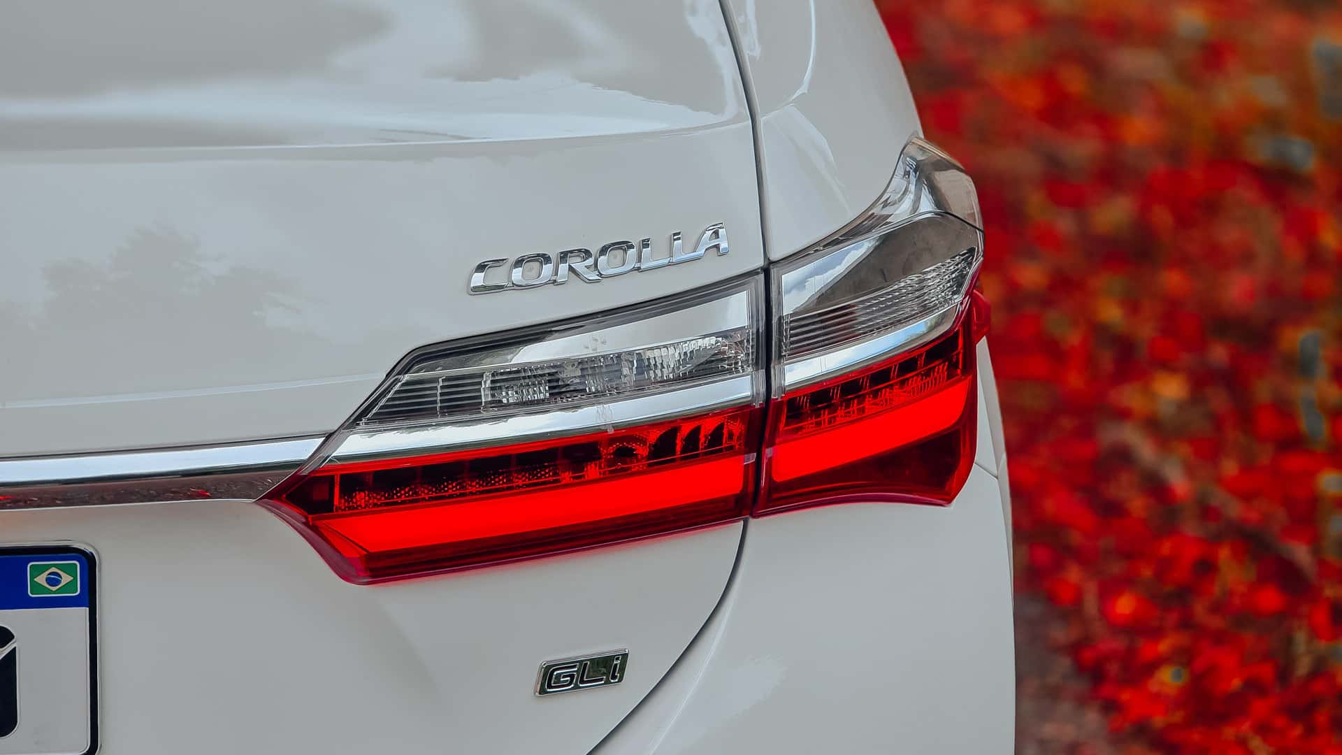 White Toyota Corolla GLi tail light and badge close-up with red autumn foliage in the background