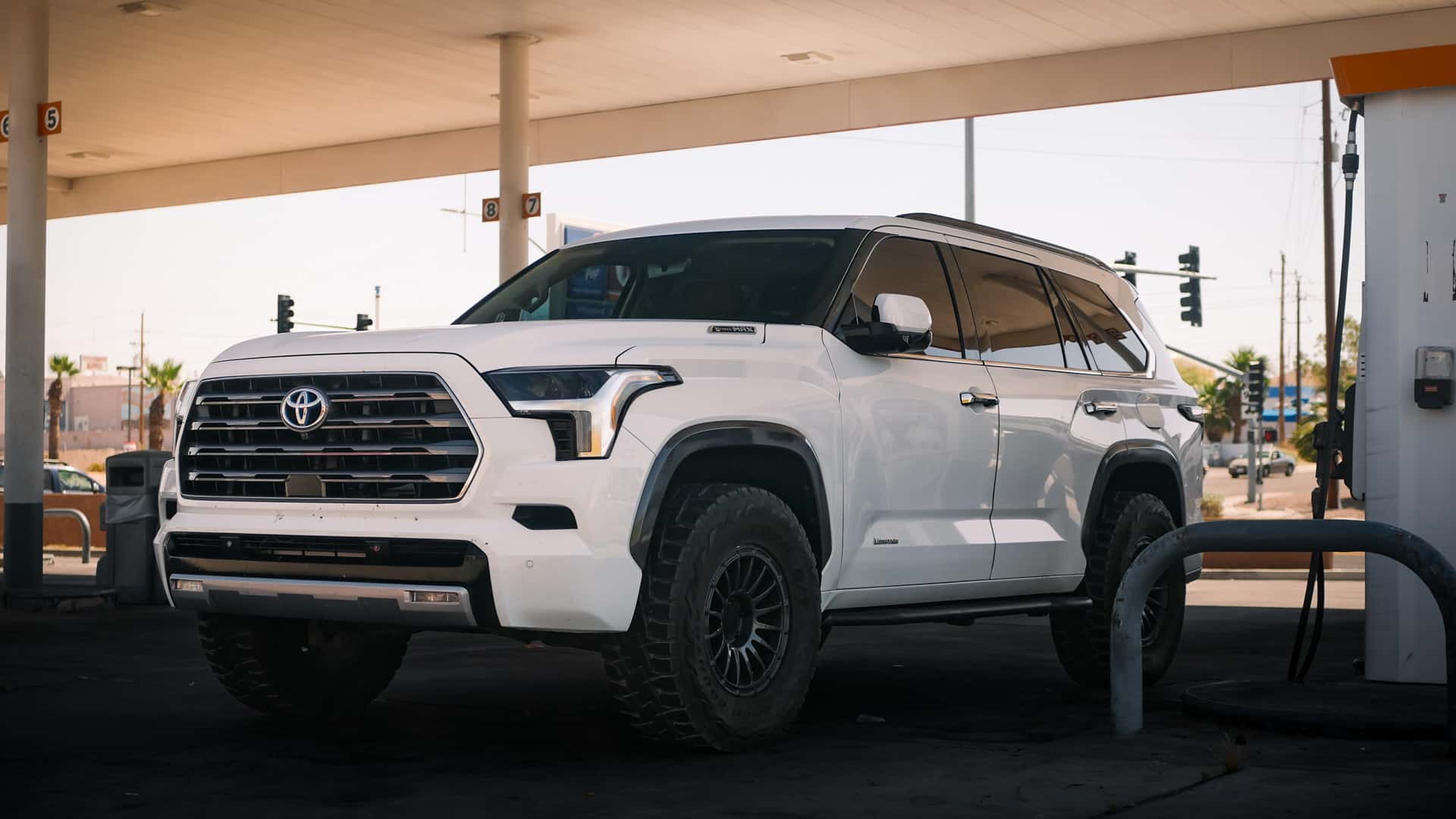 White lifted Toyota Sequoia with off-road tires parked under a gas station canopy