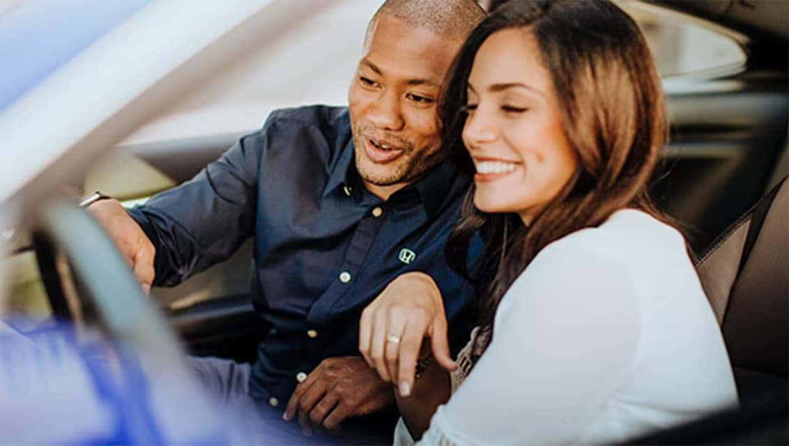 A man and woman inside a vehicle looking at the dashboard controls