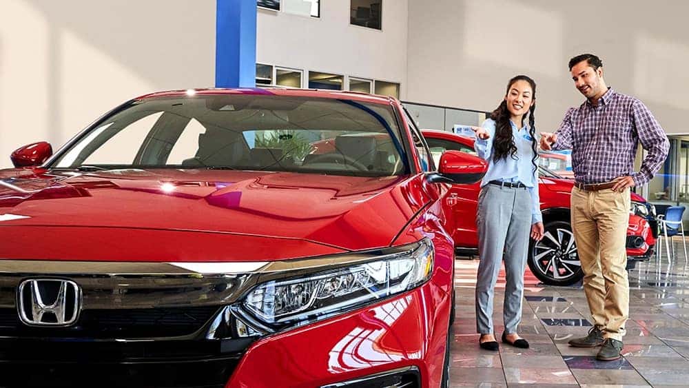 A woman and man standing next to a red Honda sedan in a dealership showroom