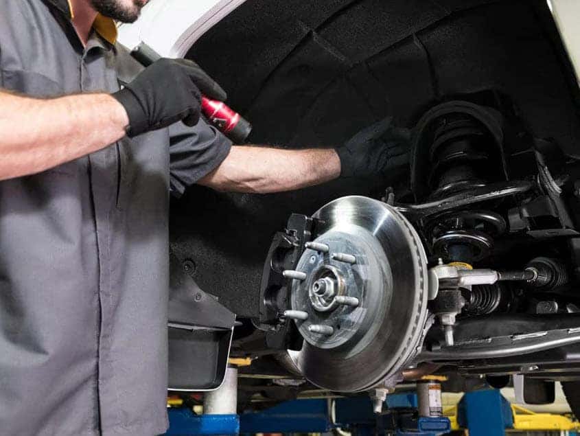 Certified technician inspecting brake system and suspension on a Buick GMC vehicle during seasonal maintenance