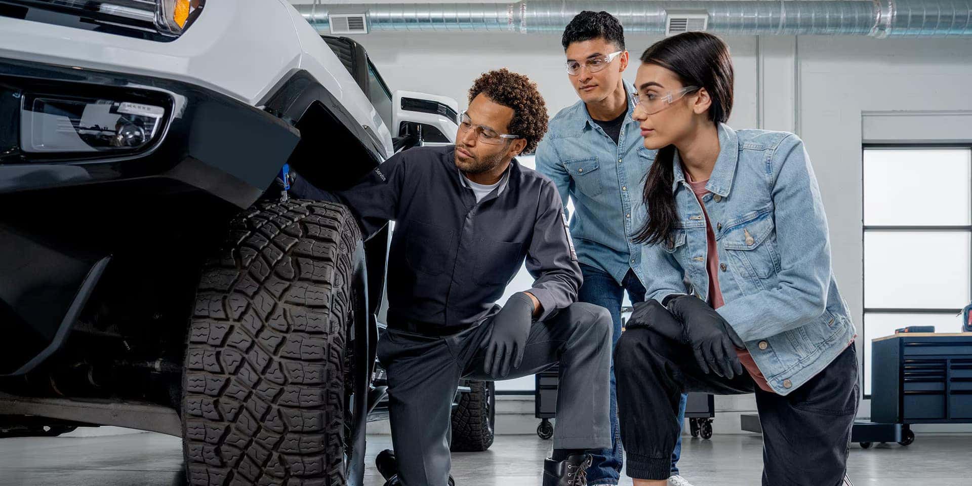 Three people inspecting the tire on a gmc.