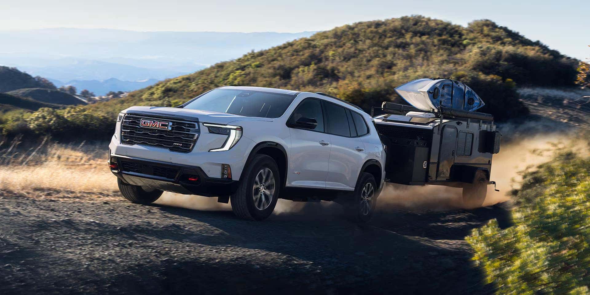 A white gmc acadia pulling a trailer off-road.