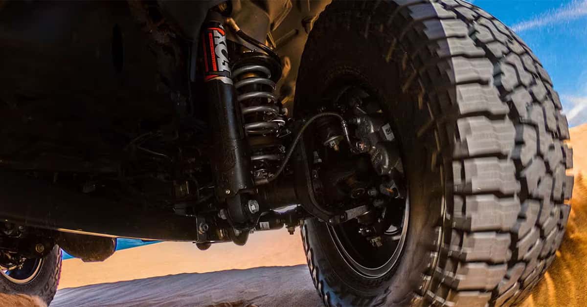 2025 Jeep Gladiator Wheel well up close with shocks and tires visible while driving over a sand dune
