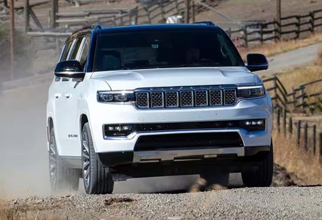 2025 Jeep Grand wagoneer driving up a hill on a farm