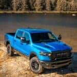 Ram1500 Rebel in two-tone Hydro Blue and Diamond Black parked on rocky riverbank surrounded by water.