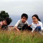 Three siblings sit on a hill at an outdoor destination for families in Marion, Illinois