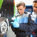 2 auto service technicians inspecting the brakes on a green car