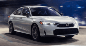 2025 Honda Civic Hybrid Sport in grey metallic paint driving at night in a city.