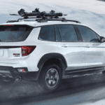 2025 Honda Passport in white paint with a roof rack driving through snowy weather conditions.