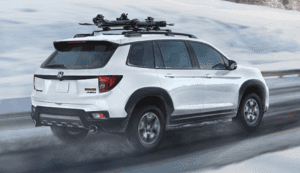 2025 Honda Passport in white paint with a roof rack driving through snowy weather conditions.