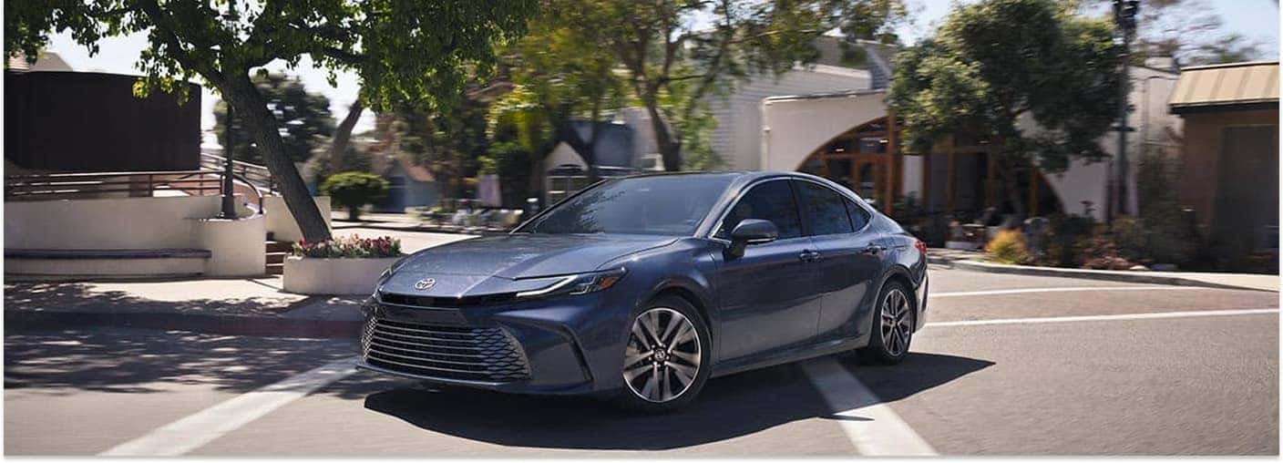 Front three-quarter view of a dark blue 2026 Toyota Camry sedan driving on a city street.