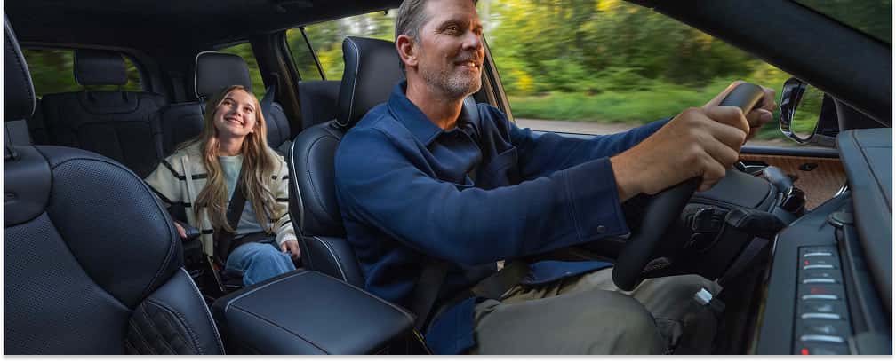 Driver and rear passenger inside the black leather interior of a 2026 Jeep Grand Cherokee L.