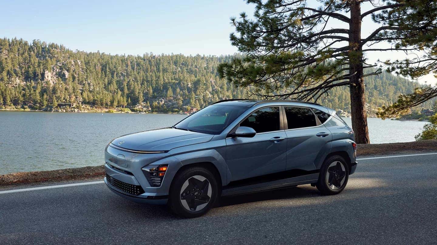 A blue Hyundai Kona driving down the road by a lake