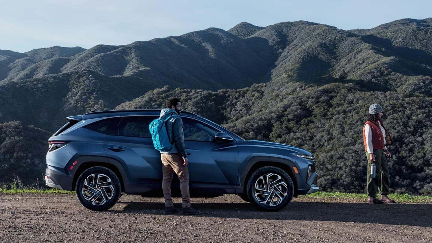 A blue Hyundai Tucson on a dirt road with a couple outside, against the backdrop of a mountain range.