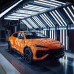 A striking orange Lamborghini Urus SE parked outdoors, showcasing its sleek design, aggressive front grille, and signature Y-shaped LED headlights. The luxury SUV features aerodynamic curves, large black alloy wheels, and a sporty stance, embodying high-performance elegance.