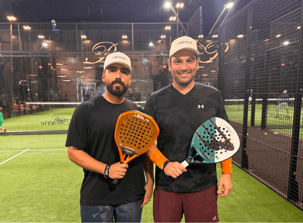 Two winners of the JLR North Dade and Reserve partnership padel tournament posing with their awards. Both winners, JLR North Dade clients, stand proudly on the court, holding their trophies with smiles, celebrating their victory in the exciting competition.