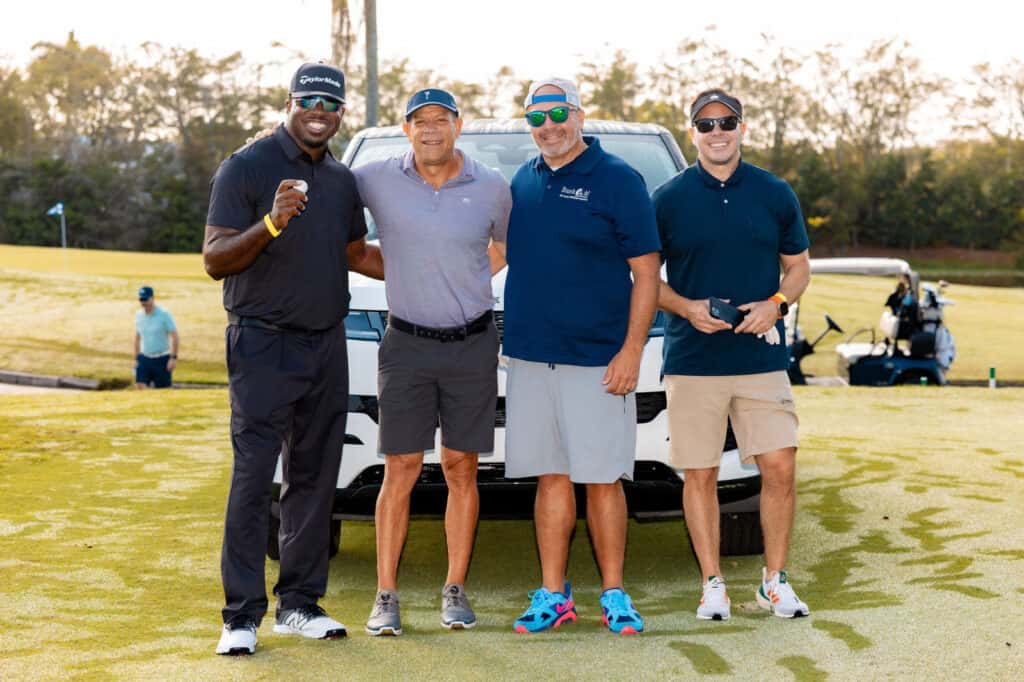 A group of four men poses together on a golf course, standing proudly in front of a white Range Rover Sport — the prize for a hole-in-one.