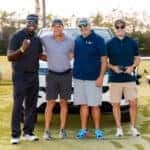 A group of four men poses together on a golf course, standing proudly in front of a white Range Rover Sport — the prize for a hole-in-one.