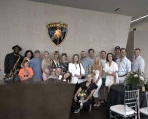 Group photo of guests smiling and posing together during the Mother's Day brunch at the Lamborghini Naples showroom, surrounded by luxury cars and elegant decor.