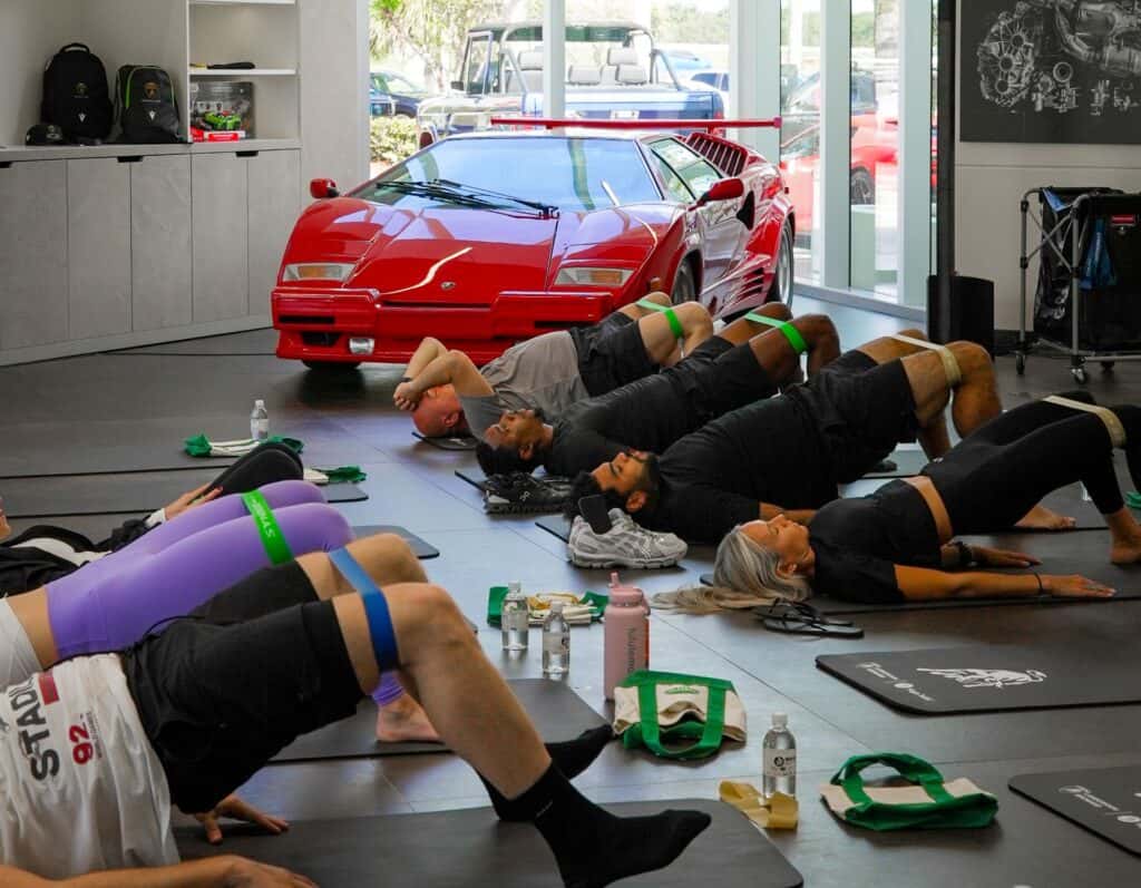 YogaJoint event attendees practicing yoga poses in front of a red vintage Lamborghini Countach inside the Lamborghini Broward showroom.
